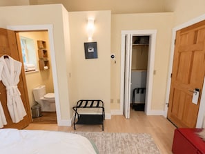 A bedroom with a bed, a bedside table, a chair, a wardrobe, a bathroom with a toilet, and a shower area.