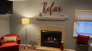 Una sala de estar acogedora con chimenea, un sillón rojo, una lámpara de pie y un letrero en la pared que dice 'Relax'.