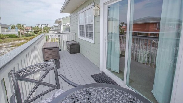 A deck with a table and chairs, a sliding glass door, and a view of neighboring houses. - Live the Salt Life in Golden Dog's Destin Rental (Destin)