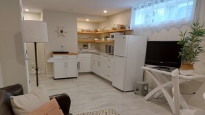 Eine moderne Küche mit weißen Geräten, ein Essbereich mit weißem Tisch und Stühlen sowie ein Wohnzimmer mit Sofa und Fernseher.