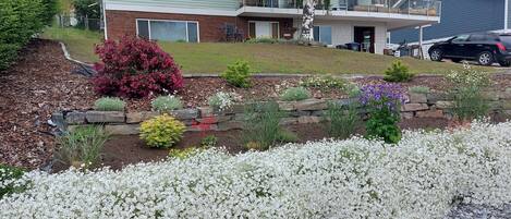 A two-story house with a front yard featuring a flower bed and a stone retaining wall.