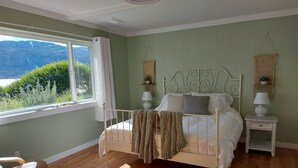 Ein Schlafzimmer mit Bett, Nachttischen, einem Sessel, einem Fenster mit Blick auf Grünflächen und Berge sowie einem Deckenventilator.