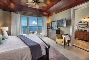 Une chambre avec un grand lit, une télévision, une commode et une vue sur l’océan.