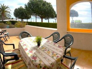 Une terrasse avec une table et des chaises, une plante en pot et une vue sur la mer.