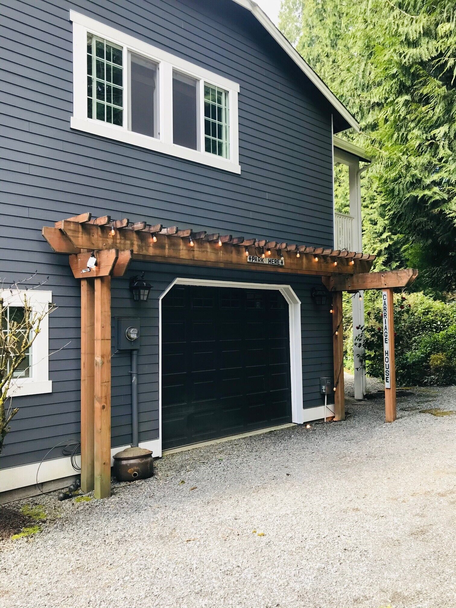 A house with a garage, a wooden pergola with lights, and a sign that says 'PARK HERE'.