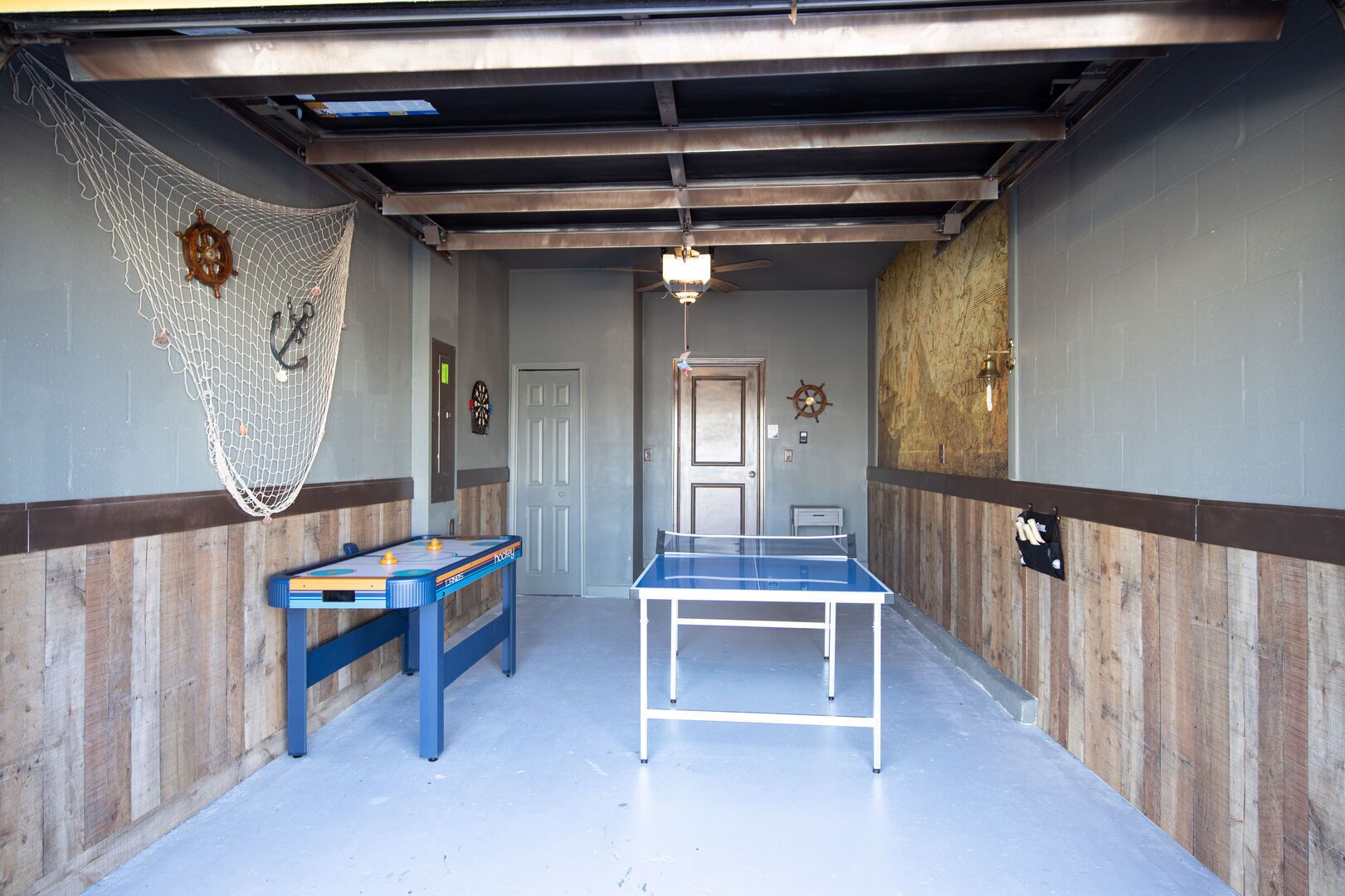 A room with a ping pong table, a foosball table, and a netted area.