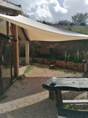 Ein überdachter Außenbereich mit Tisch und Stuhl, einer Steinmauer und einer Holzterrasse.