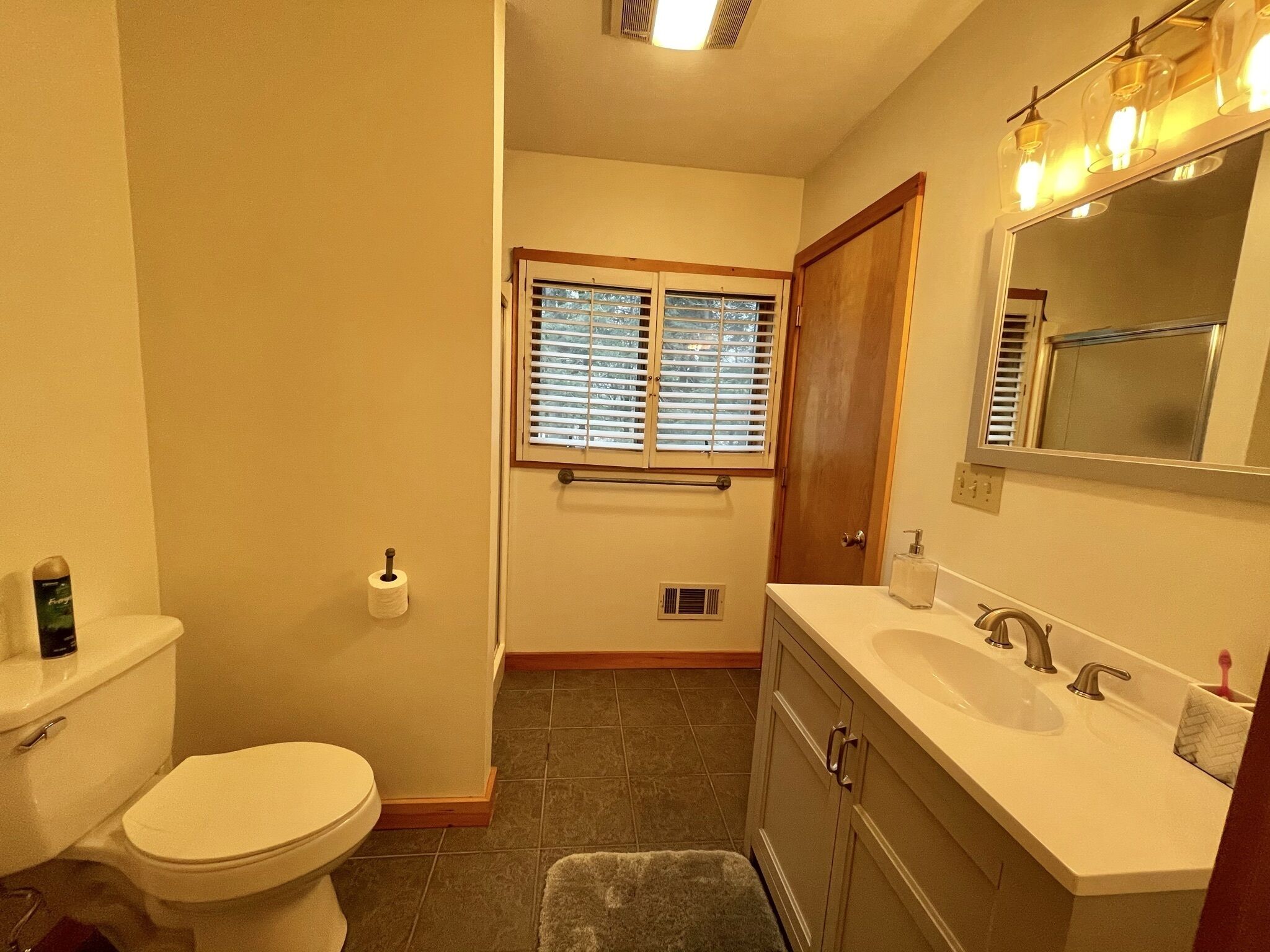 Ein Badezimmer mit Toilette, Waschbecken, Waschtisch und einem Fenster mit Jalousien.