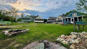 A grassy area with a stone wall and rocks, surrounded by buildings with a porch and a covered area. - Heron Lodge - The Lodges at Oak Point, 1000 Islands - Right on the River! (Hammond)