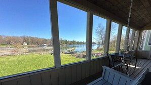 A covered porch with a view of a lake and grassy area. - Heron Lodge - The Lodges at Oak Point, 1000 Islands - Right on the River! (Hammond)
