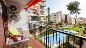 Un balcon avec une table dressée pour le dîner, une piscine et une vue sur les bâtiments environnants.