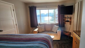Quarto com cama, sofá-cama, televisão e janela com vista para as montanhas.