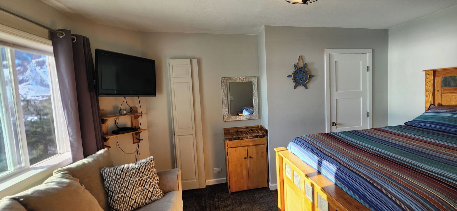 A bedroom with a bed, a television, a wardrobe, a mirror, and a window.