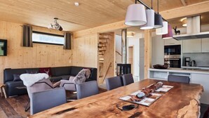 A modern interior with a wooden dining table, grey sofas, and a kitchen area.