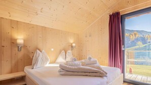 A wooden-paneled bedroom with a bed, two wall-mounted lamps, and a large window with a view of the outdoors.