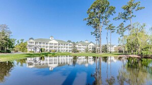 Un grand hôtel à plusieurs étages, avec un bassin d’eau aux reflets changeants à l’avant, entouré d’arbres et d’une pelouse bien entretenue.