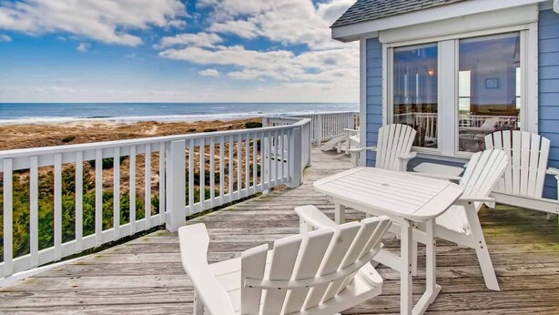 A wooden deck with white chairs and a table, overlooking the ocean. - Premier Oceanfront Carolina Dreamin’ w/ Pool, Hot Tub, Elevator, Game Room (Avon)