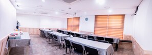 A conference room with multiple tables and chairs, wooden paneling, and a clock on the wall. - Hotel BELLIA (Busan)