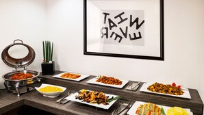 A buffet table with various dishes, a framed sign on the wall, and a decorative plant. - Hotel BELLIA (Busan)