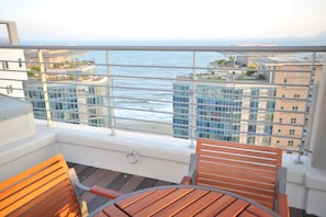 A balcony with a view of the ocean and buildings. There are wooden chairs and a table. - Hotel BELLIA (Busan)