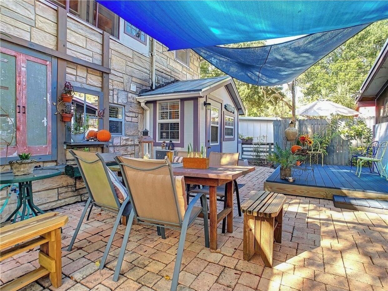 Eine Terrasse im Freien mit Tisch und Stühlen, ein Holzdeck und ein blaues Sonnensegel.
