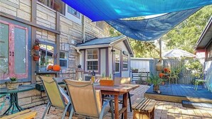 Um pátio externo com mesa e cadeiras, um deck de madeira e uma vela de sombreamento azul.