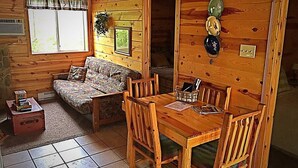 Ein gemütliches Blockhaus-Interieur mit einem Holzesstisch, Stühlen, einer Couch und einer kleinen Küchenzeile.