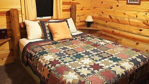 Ein holzgetäfeltes Zimmer im Chalet-Stil mit Bett, Nachttisch, Lampe und einem gerahmten Bild an der Wand.