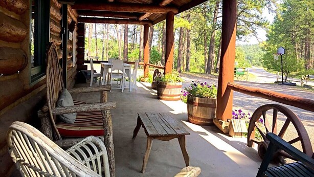 A log cabin with a porch, wooden furniture, and potted plants. - One Bedroom Cabin near Mount Rushmore (Rapid City)