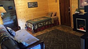 A cozy log cabin room with a bed, a couch, a fireplace, and an exit sign. - One Bedroom Cabin near Mount Rushmore (Rapid City)