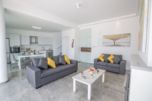 A modern living room with two grey sofas, a white coffee table, and a dining area with a glass table and chairs.