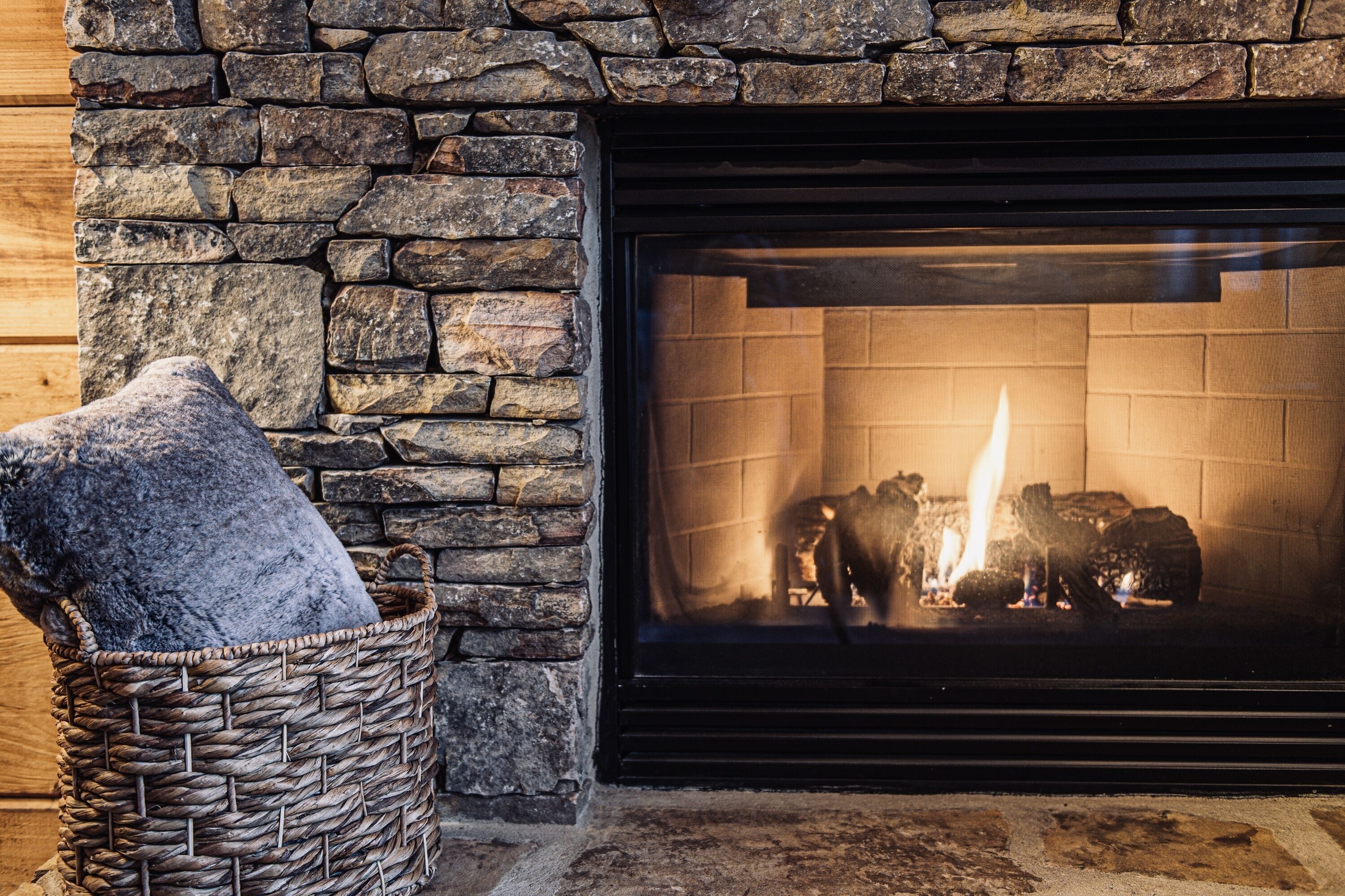 A stone fireplace with a basket and a cushion.