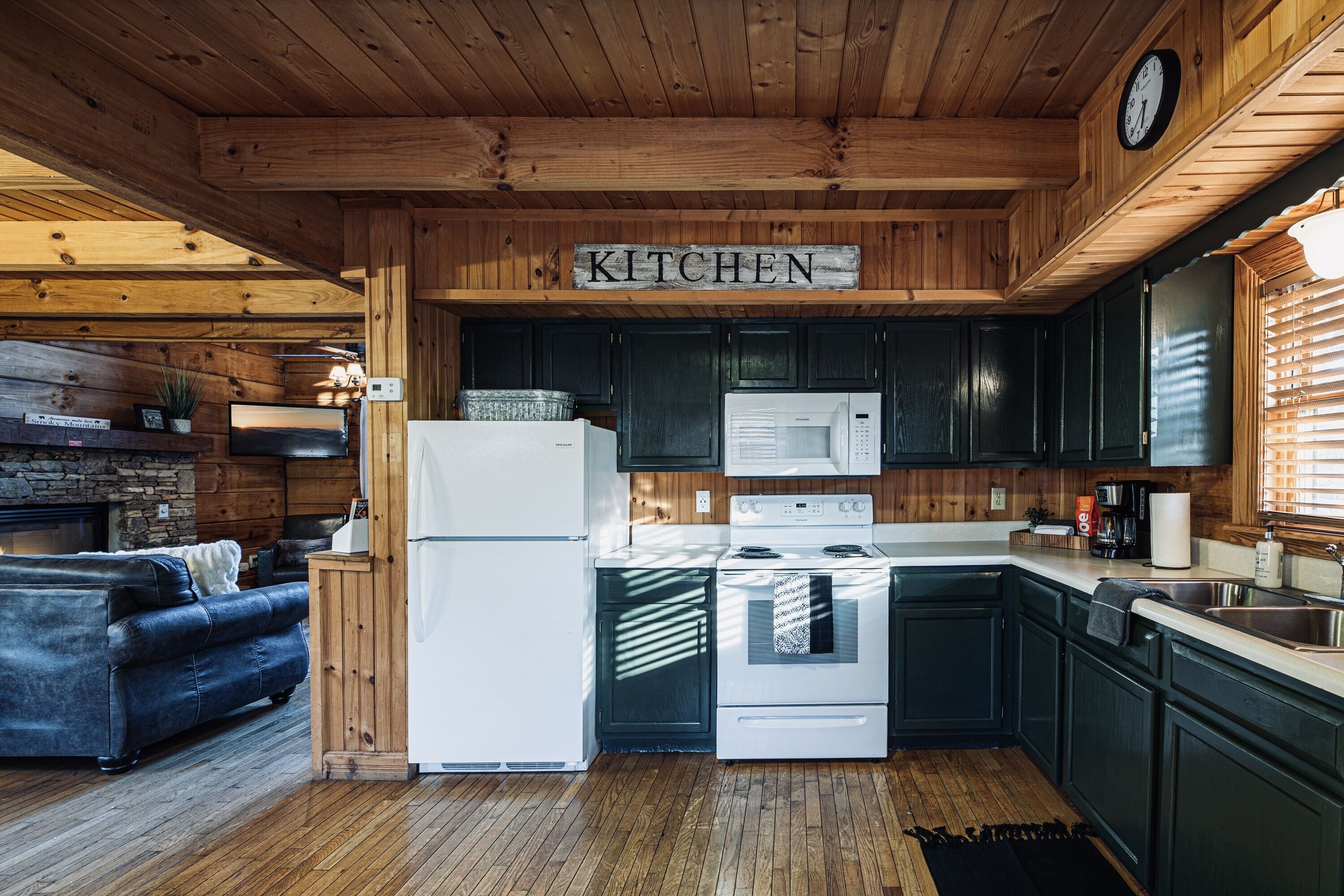 A wooden interior with a kitchen area featuring a refrigerator, microwave, stove, and dark cabinets.