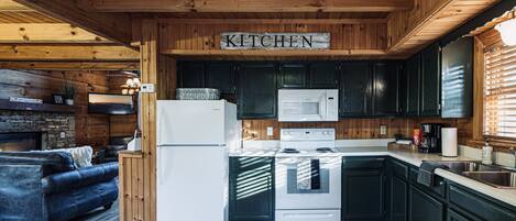 A wooden interior with a kitchen area featuring a refrigerator, microwave, stove, and dark cabinets.