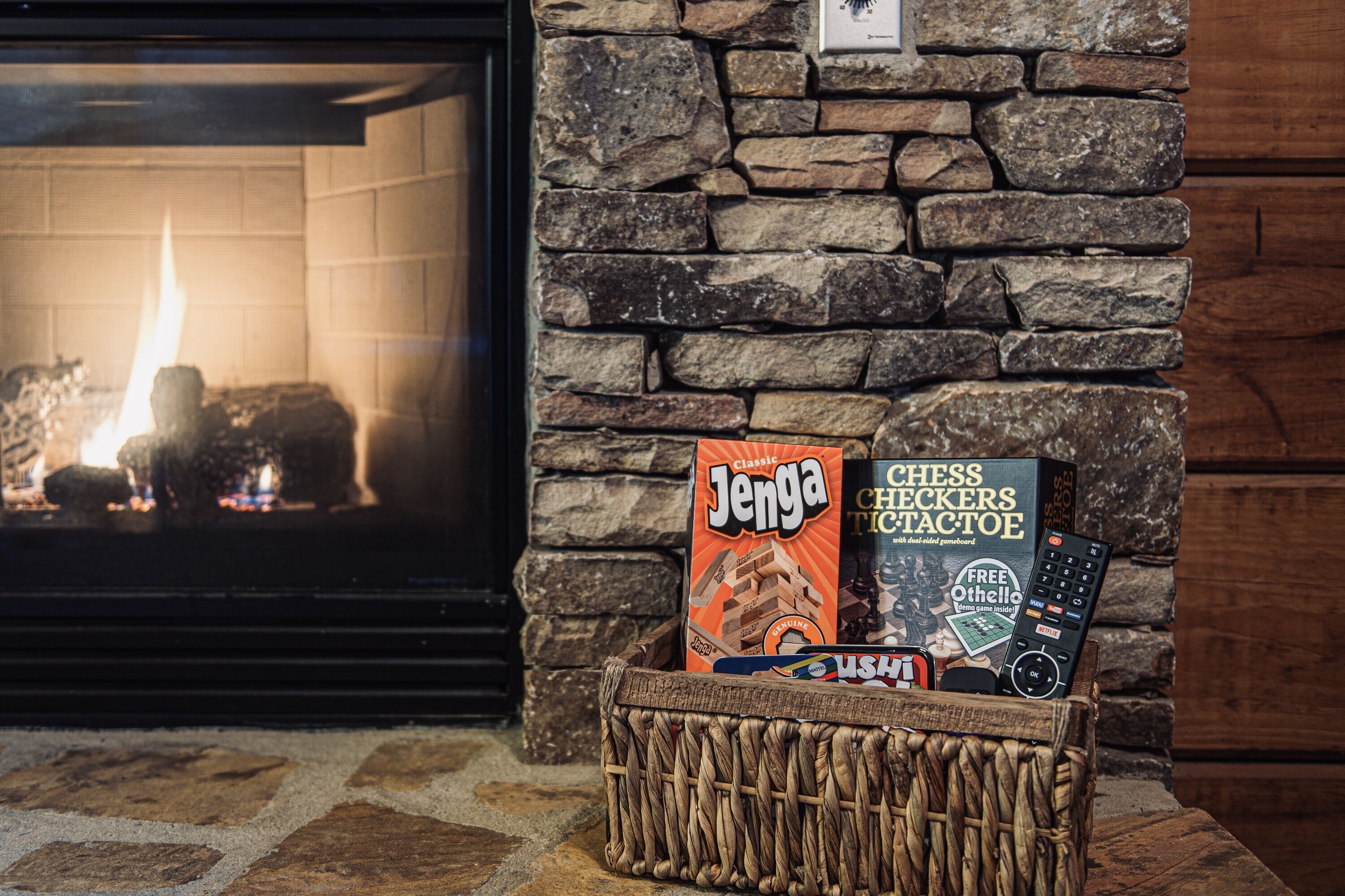 A stone fireplace with a fire, a basket containing board games, and a television.