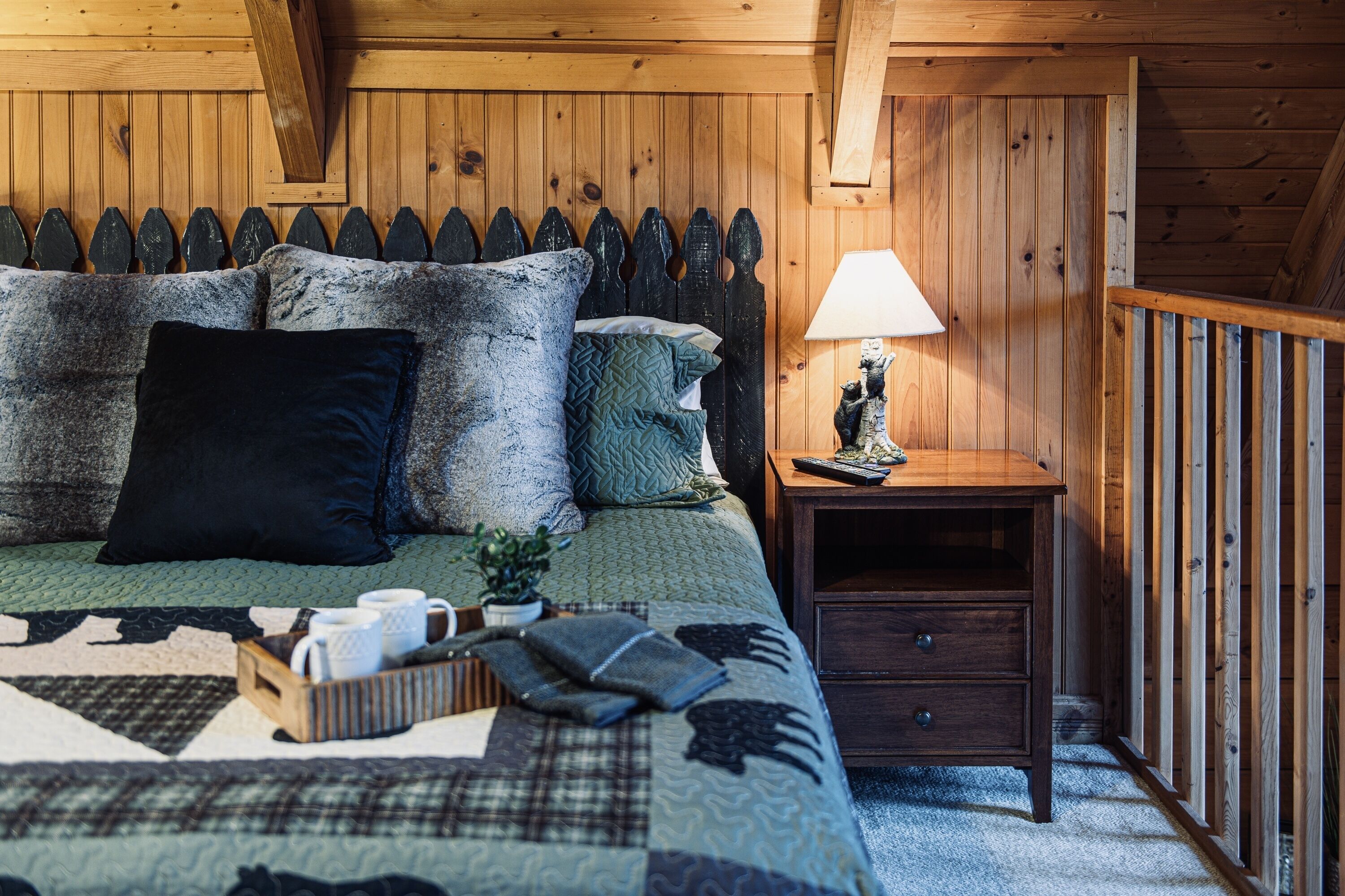Una camera accogliente con soffitto in legno, un letto con copriletto, cuscini, un comodino con una lampada e una piccola pianta.