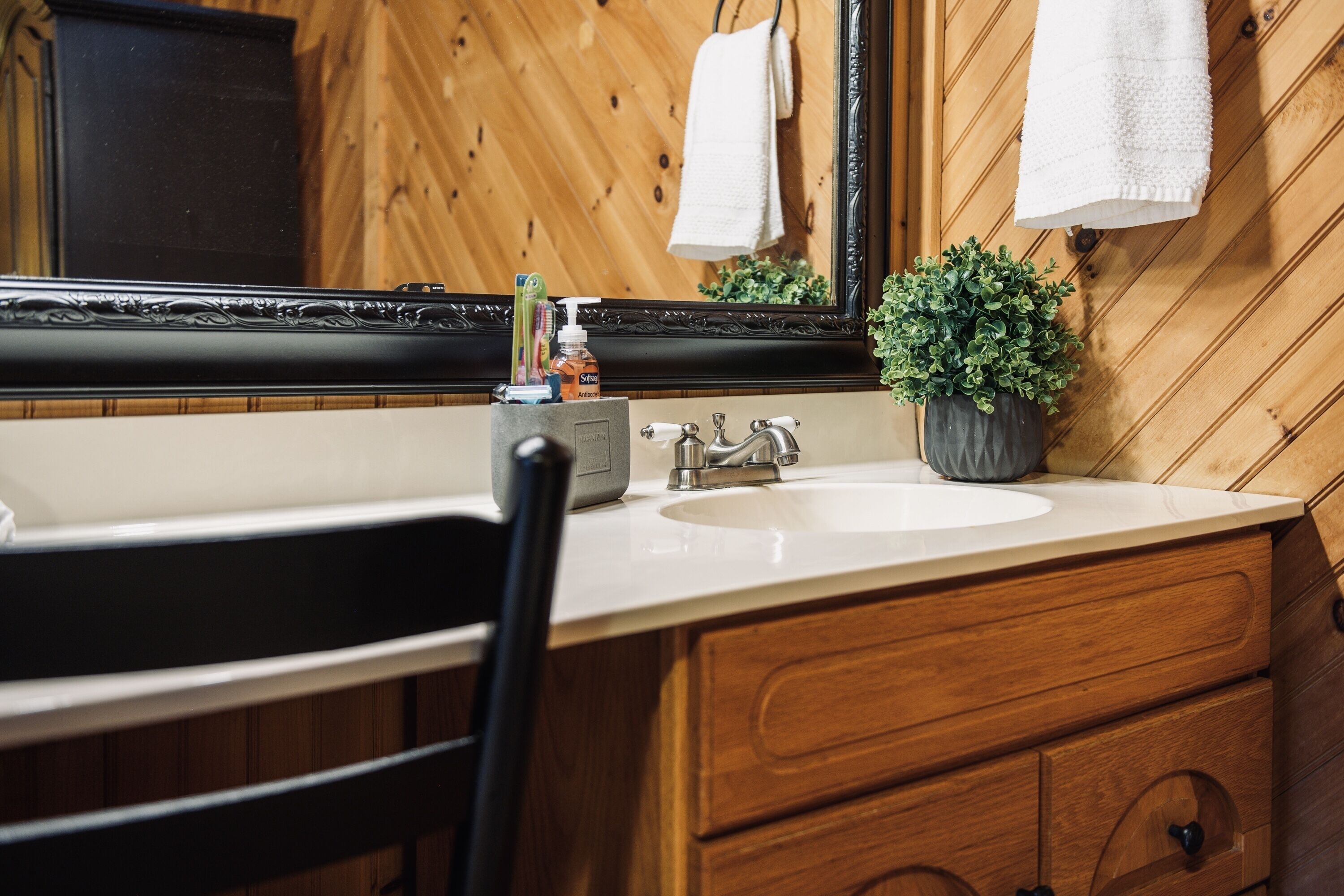 A wooden-paneled bathroom with a white sink, a black chair, and a potted plant.