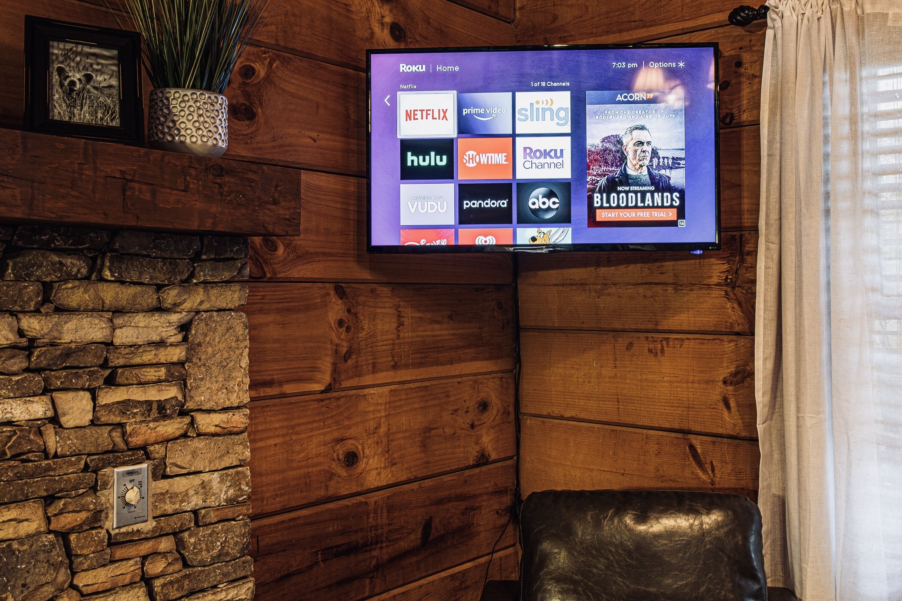 A flat-screen TV mounted on a wooden wall displaying a streaming service interface with various channel logos.