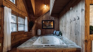 A wooden cabin interior with a stone bathtub, wooden walls, and a window with curtains. - Bear Cavern *Minutes to Main Pigeon Forge Pkwy* (Pigeon Forge)