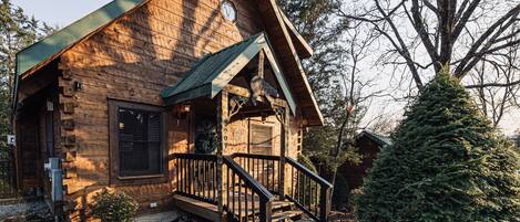 A rustic log cabin with a wooden exterior, a front porch, and a staircase leading to the entrance.