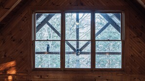 A wooden cabin with a large window framed by wooden beams, offering a view of snow-covered trees. - Bear Cavern *Minutes to Main Pigeon Forge Pkwy* (Pigeon Forge)