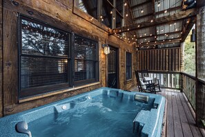 Une terrasse en bois avec un jacuzzi, de grandes fenêtres et des guirlandes lumineuses.