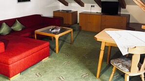 Une pièce confortable de style loft, avec un canapé rouge, une table basse en bois, une table à manger avec une chaise et un téléviseur posé sur un meuble en bois.