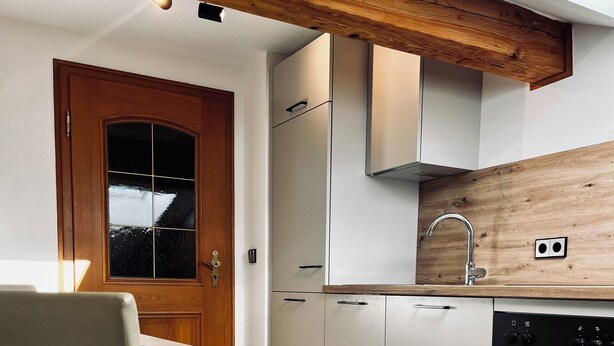 Une cuisine moderne avec un plafond en bois, des armoires blanches, un four encastré et un coin repas comprenant une chaise et une table.