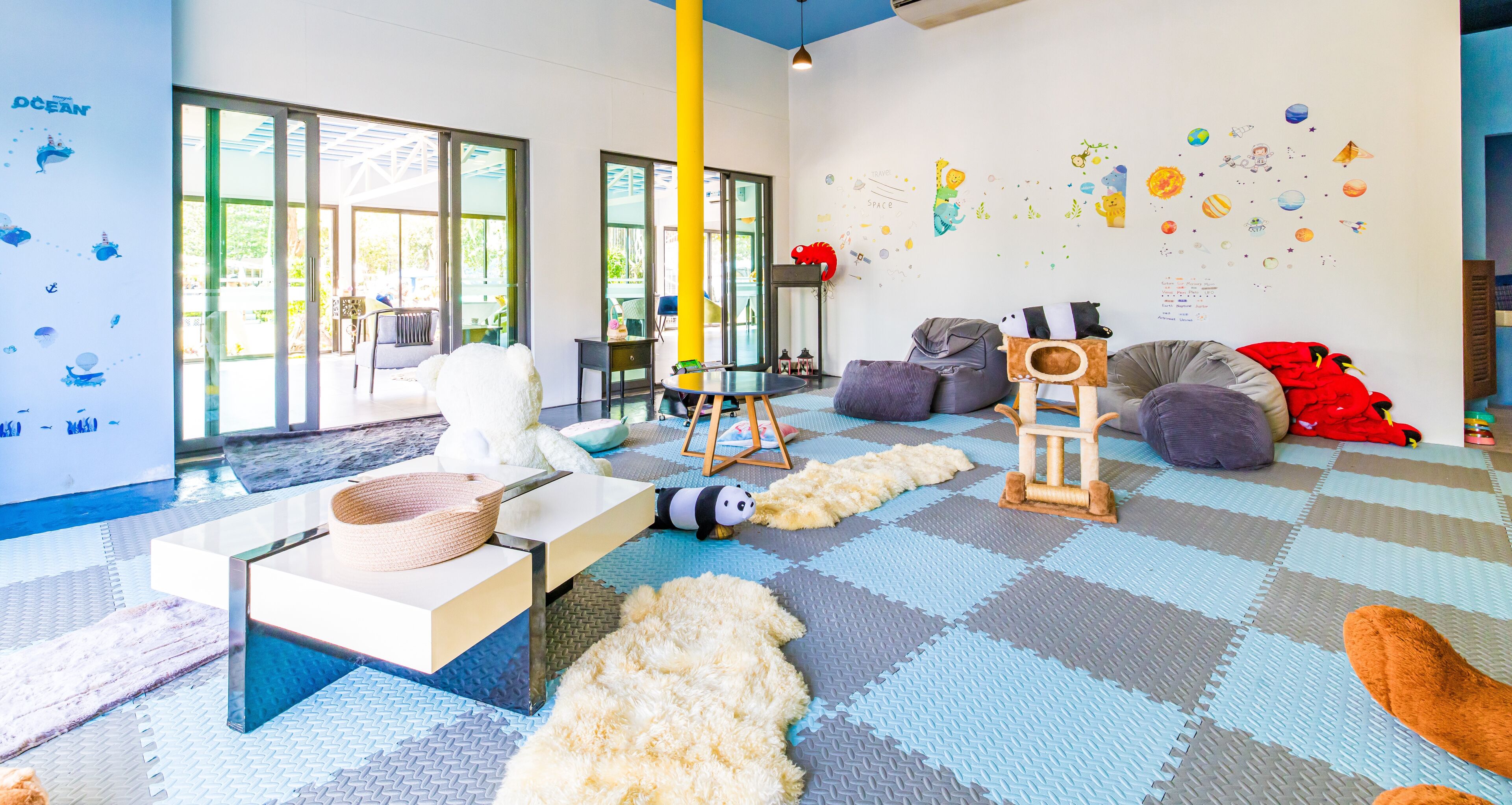 Une pièce conçue pour les enfants, avec un espace de jeux comprenant une table, un panier en osier, un ours en peluche à l'effigie d'un panda et un grand poteau jaune.