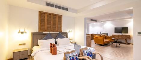 A modern hotel room with a large bed, a desk, a sofa, and a television.