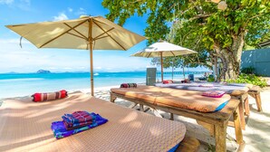 A beachside lounge with wooden tables and beige umbrellas, overlooking a clear blue sea and a distant island. - Royal Yao Yai Island Beach Resort -sha Extra Plus+ (Ko Yao)