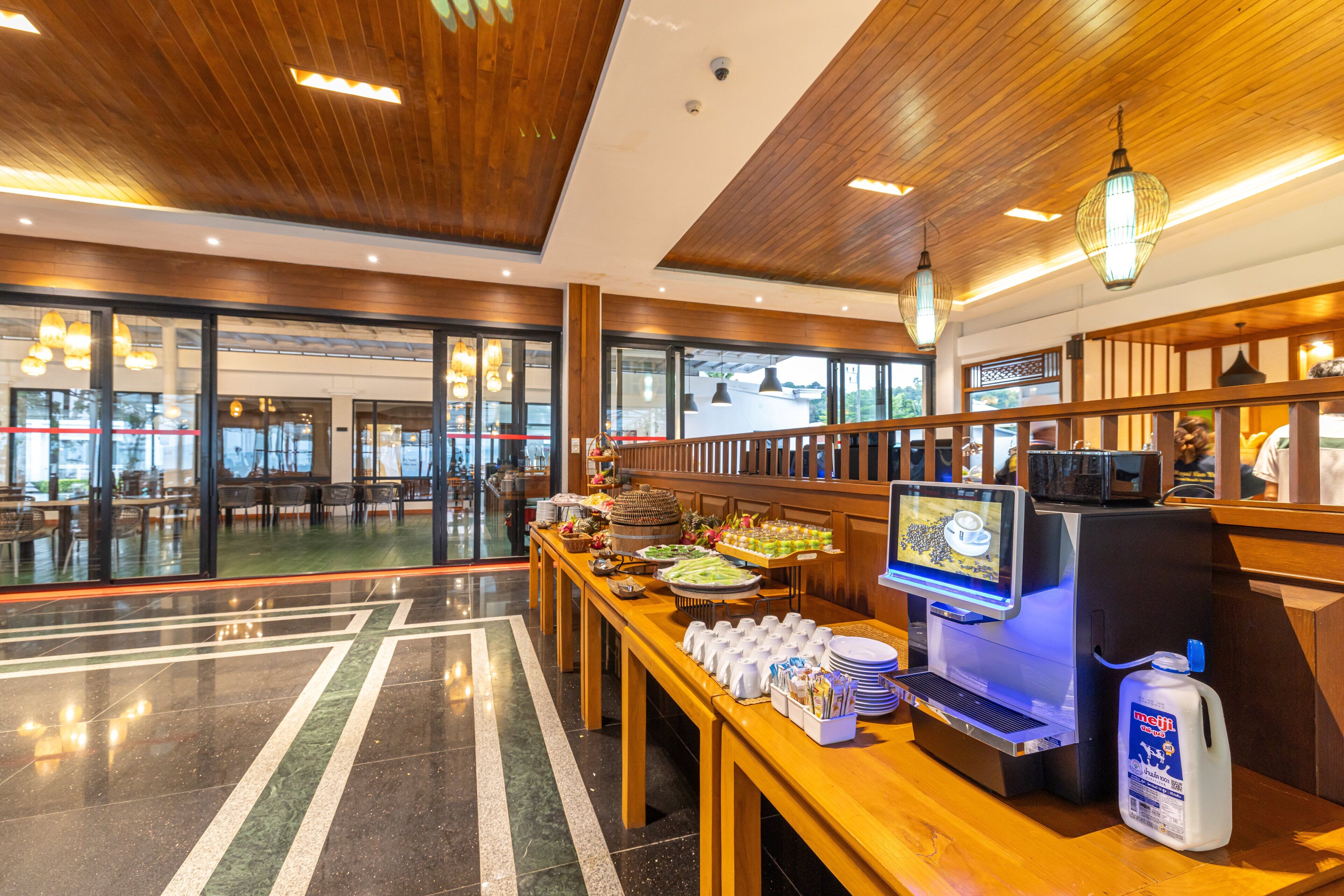 A modern hotel lobby with a buffet area, wooden flooring, and a digital kiosk.