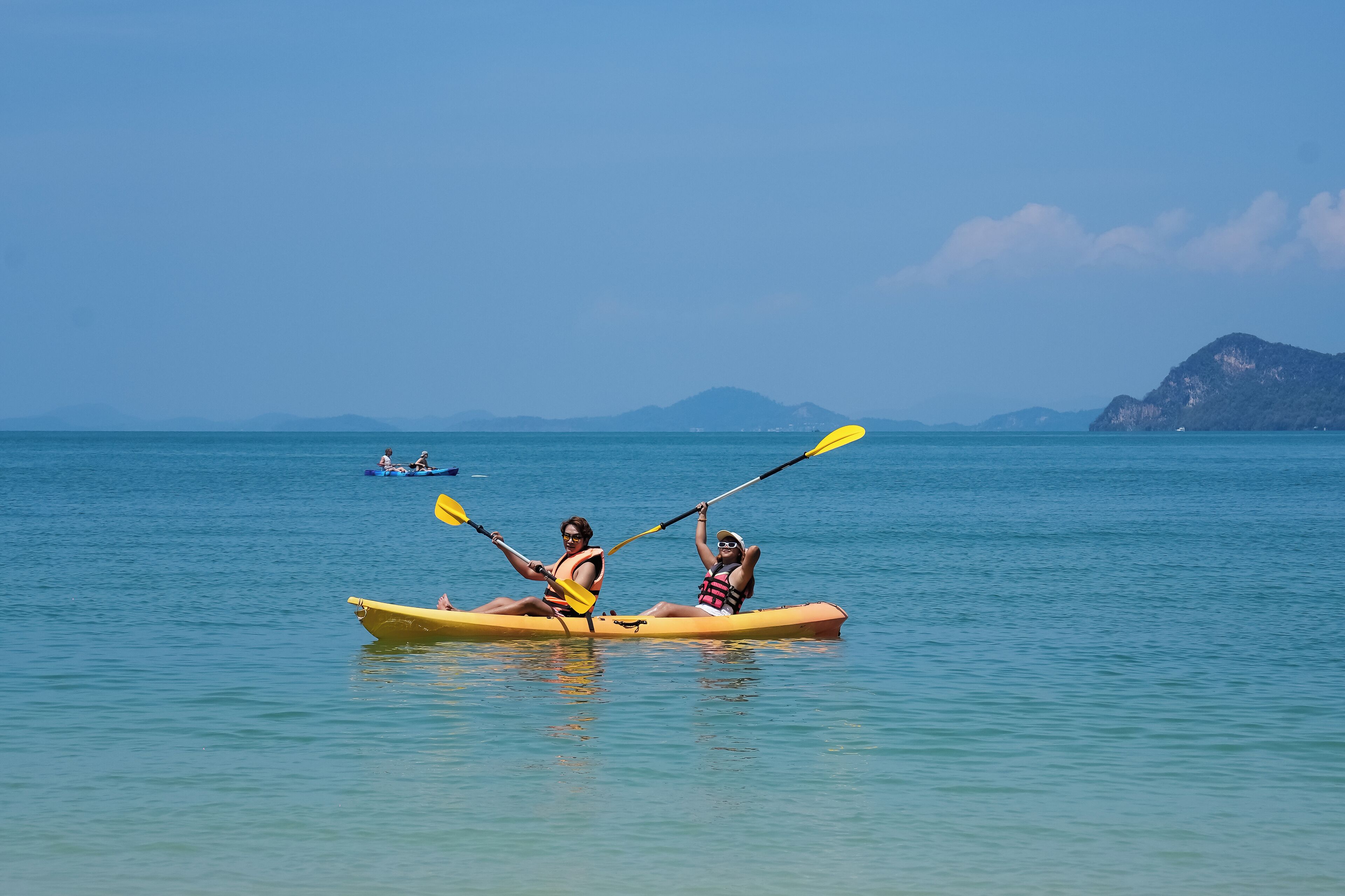 Dos personas haciendo kayak en un mar tranquilo con montañas a lo lejos.