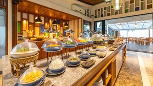 A buffet with various food items covered in dome lids, a wooden ceiling, and a view of the outdoor area. - Royal Yao Yai Island Beach Resort -sha Extra Plus+ (Ko Yao)